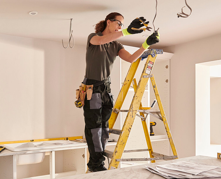 electrician on a ladder installing lights in ceiling