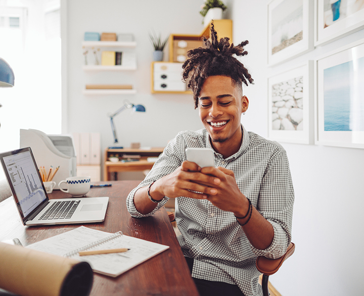 smiling guy sitting at a desk and looking at his phone