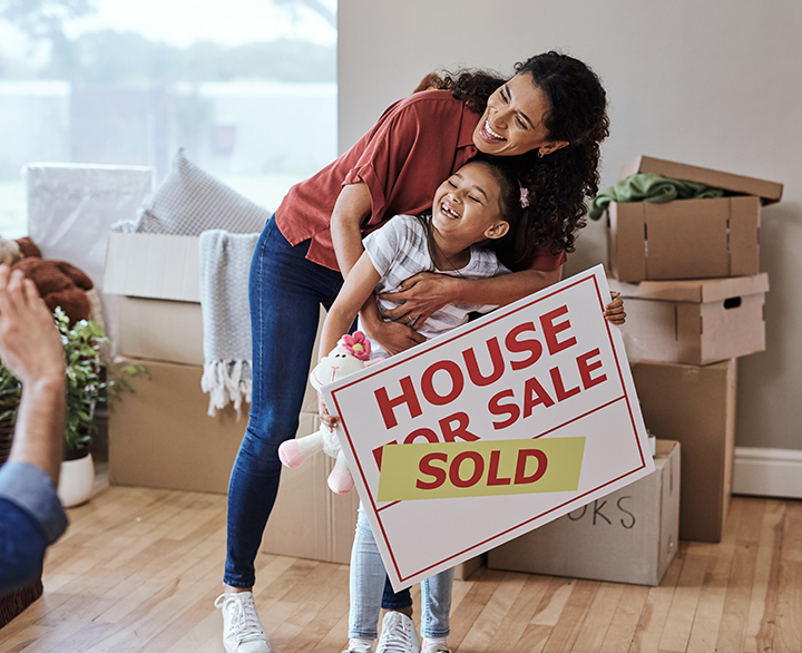 mother and young daughter holding a house sign with a SOLD sticker on it
