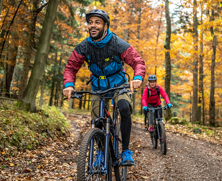 man and woman mountain biking through a forest in autumn