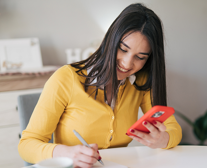 woman holding a phone and writing a note