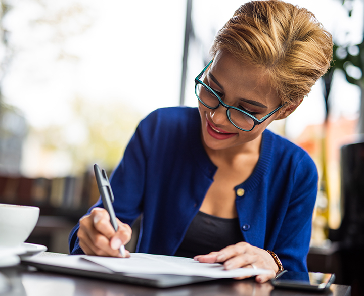 woman in glasses writing by hand at a cafe
