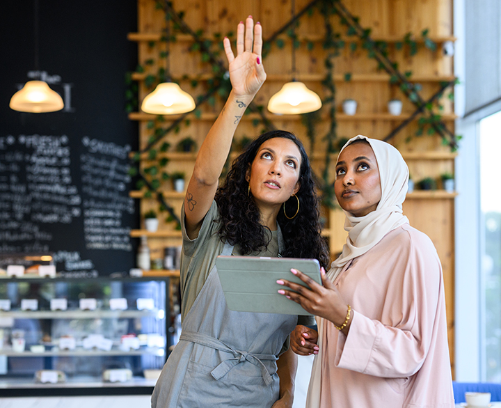 two women in a cafe with a tablet looking up at something