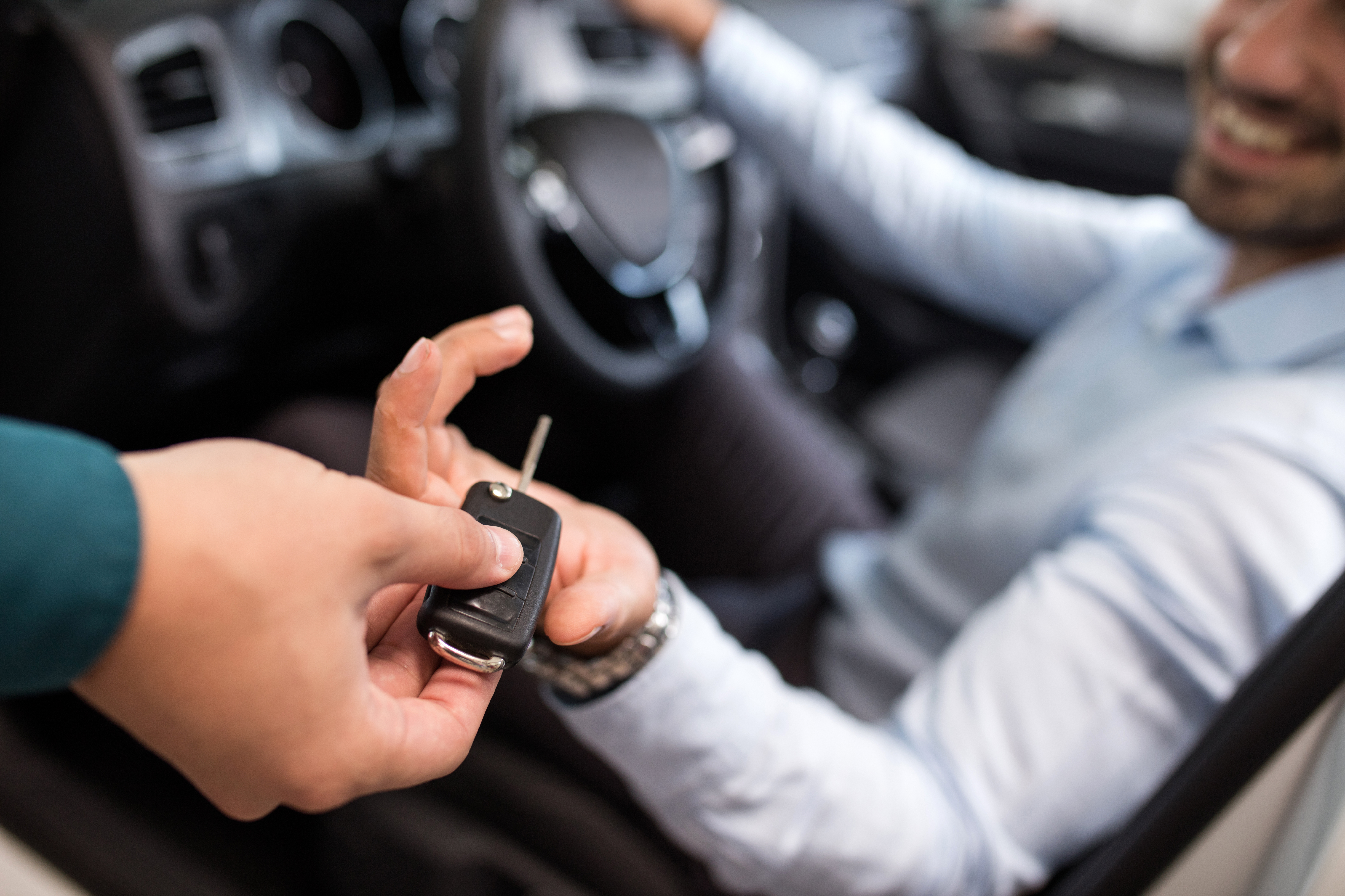 Close up of a man sitting in a car and receiving car keys from unrecognizable person.