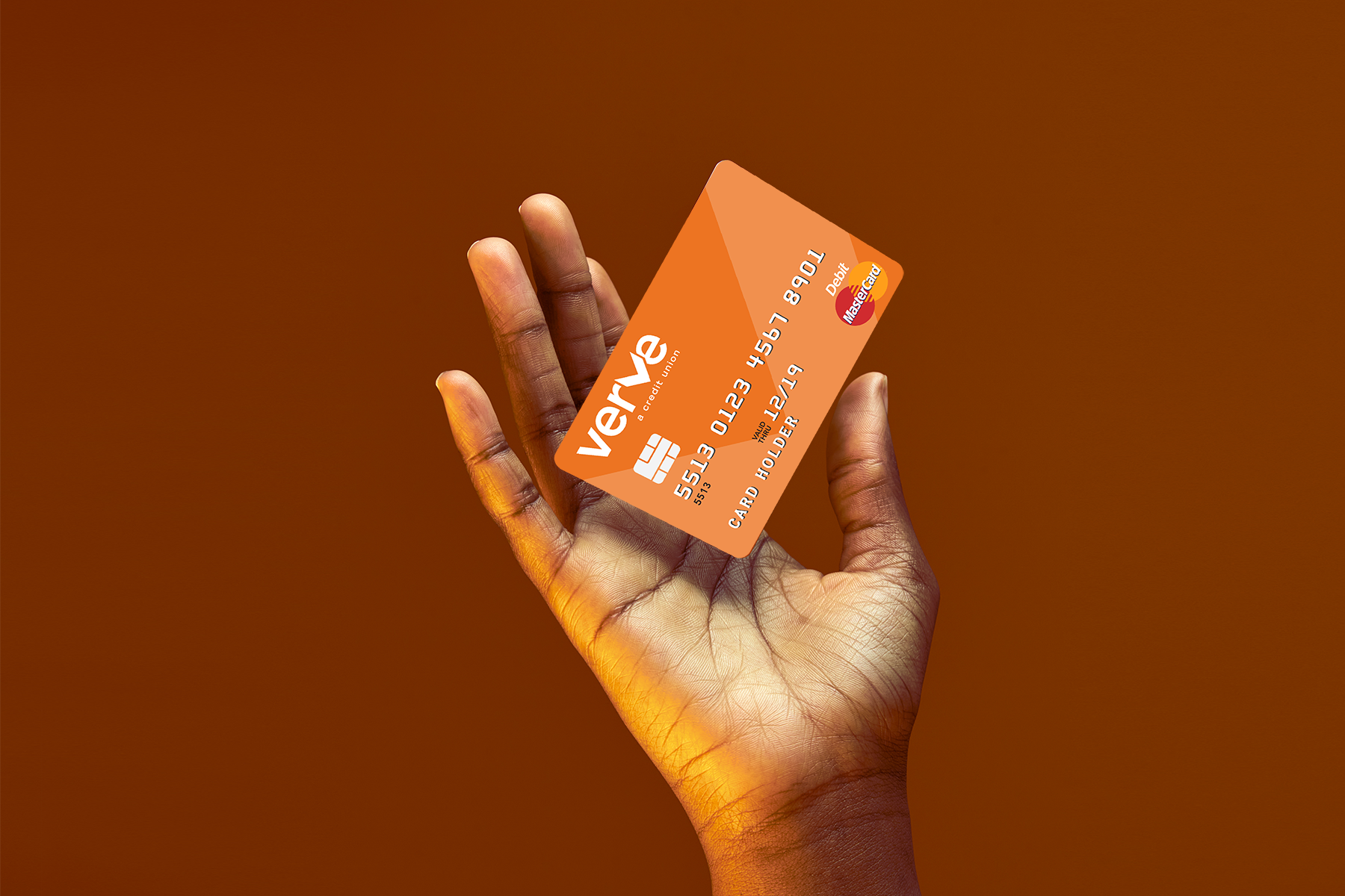 Hand holding orange Verve debit card on dark orange background