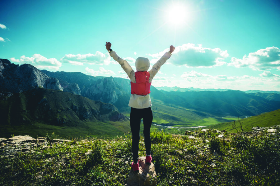 Successful woman backpacker hiking on sunset alpine mountain peak